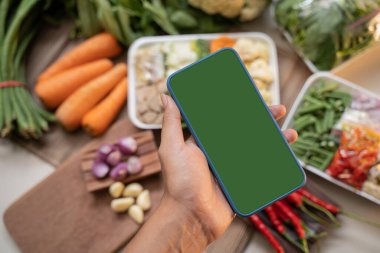Sebze geçmişi olan akıllı bir telefonu tutan eller.