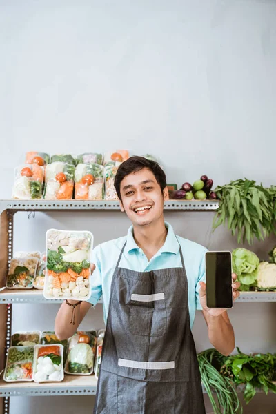 Aziatische man groenteboer tonen groenten en tonen een telefoon scherm — Stockfoto