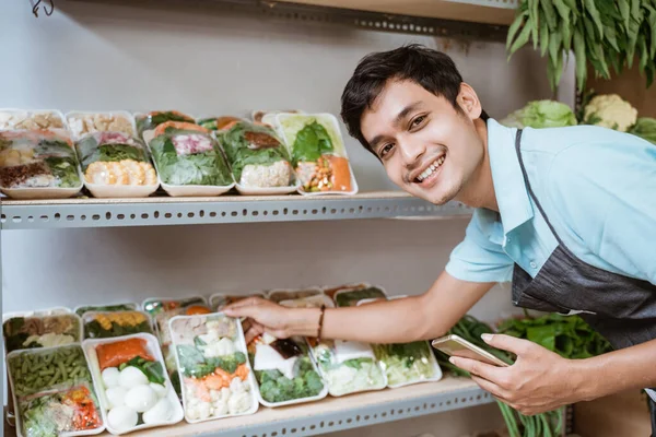 Glimlachende man die groenten verkoopt met een smartphone terwijl hij groenten controleert — Stockfoto