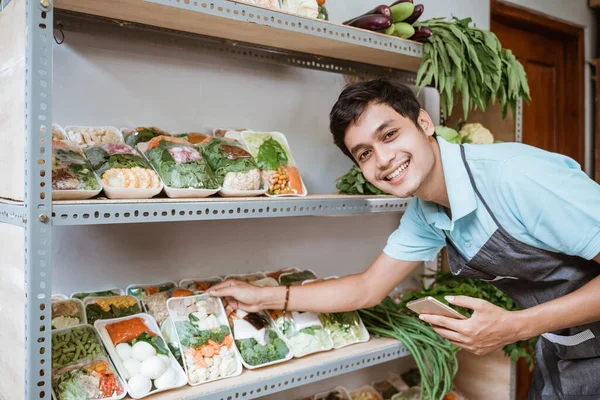 Glimlachende man verkoopt groenten met een mobiele telefoon tijdens het controleren — Stockfoto