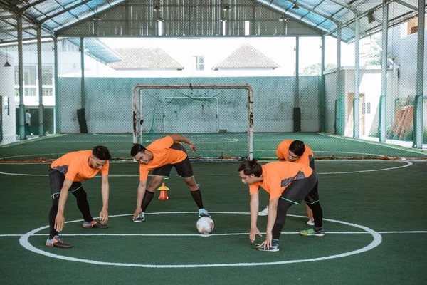 Czterech futsal graczy rozciągających nogi na środku boiska — Zdjęcie stockowe