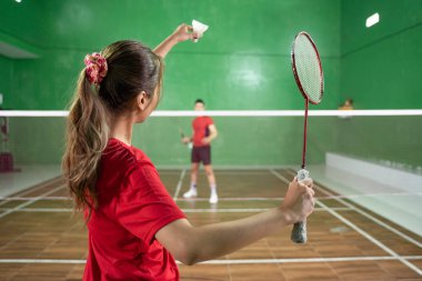 Bayan badminton oyuncusu servis pozisyonunda mekik ve raket tutuyor.