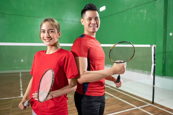 Dois jogadores de badminton sorridentes segurando raquetes de costas para trás — Fotografia de Stock