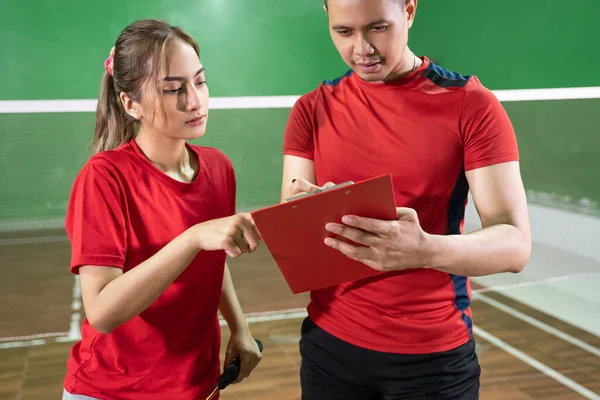 Female badminton player communicating with male coach with clipboard — Stock Photo, Image