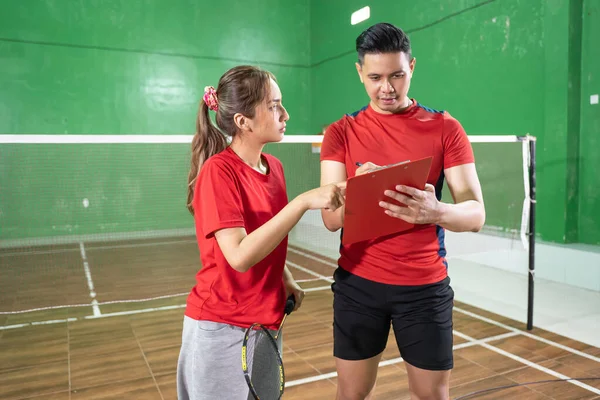 Vrouwelijke badminton speler gegeven instructies door mannelijke coach met klembord — Stockfoto