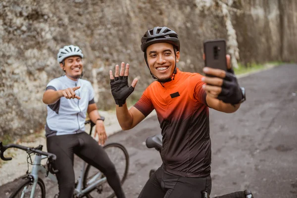 Ciclista masculino sentado en bicicleta y usando el teléfono para tomar selfie o videollamadas — Foto de Stock