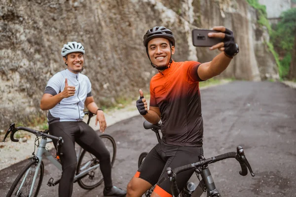 Ciclista masculino sentado en bicicleta y usando el teléfono para tomar selfie o videollamadas — Foto de Stock