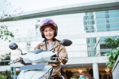 Motosiklet süren Asyalı kadın kask takıyor.