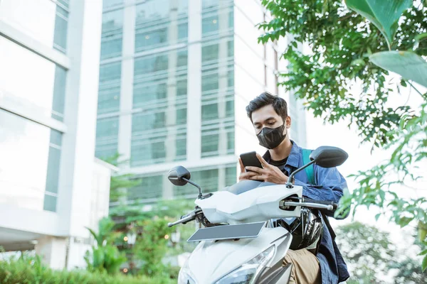 오토바이에 휴대폰을 사용하여 마스크를 쓴 아시아 남자 — 스톡 사진