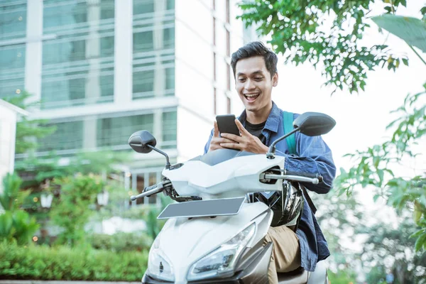 Smiling asian man using a cellphone while riding a motorcycle — Stock Photo, Image