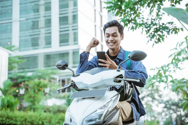 Excited asian man using a cellphone while riding a motorcycle — Stock Photo, Image
