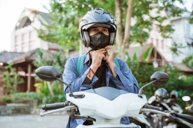 Adam motosiklette kask ve maske takmaya hazırlanıyor.