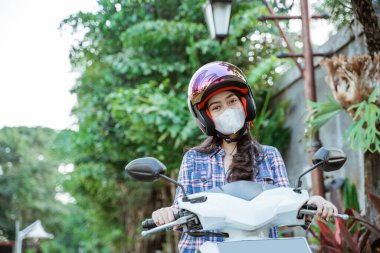 Motosiklette kask ve maske takan Asyalı kadın.