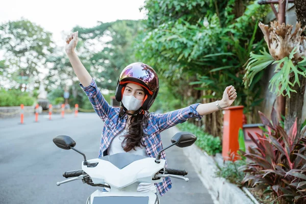 Возбужденная женщина поднимает руки с помощью шлема и маски на мотоцикле — стоковое фото