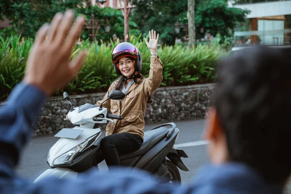 헬멧을 쓰고 오토바이를 타고 누군가와 손을 흔들고 있는 여자 — 스톡 사진