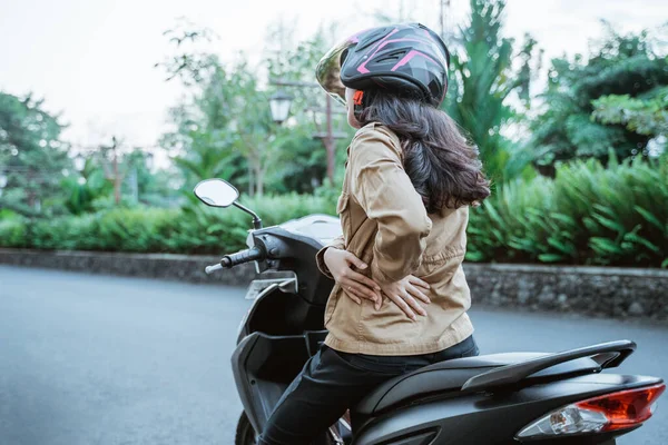Woman wearing helmet stops riding motorbike due to back pain — Stock Photo, Image