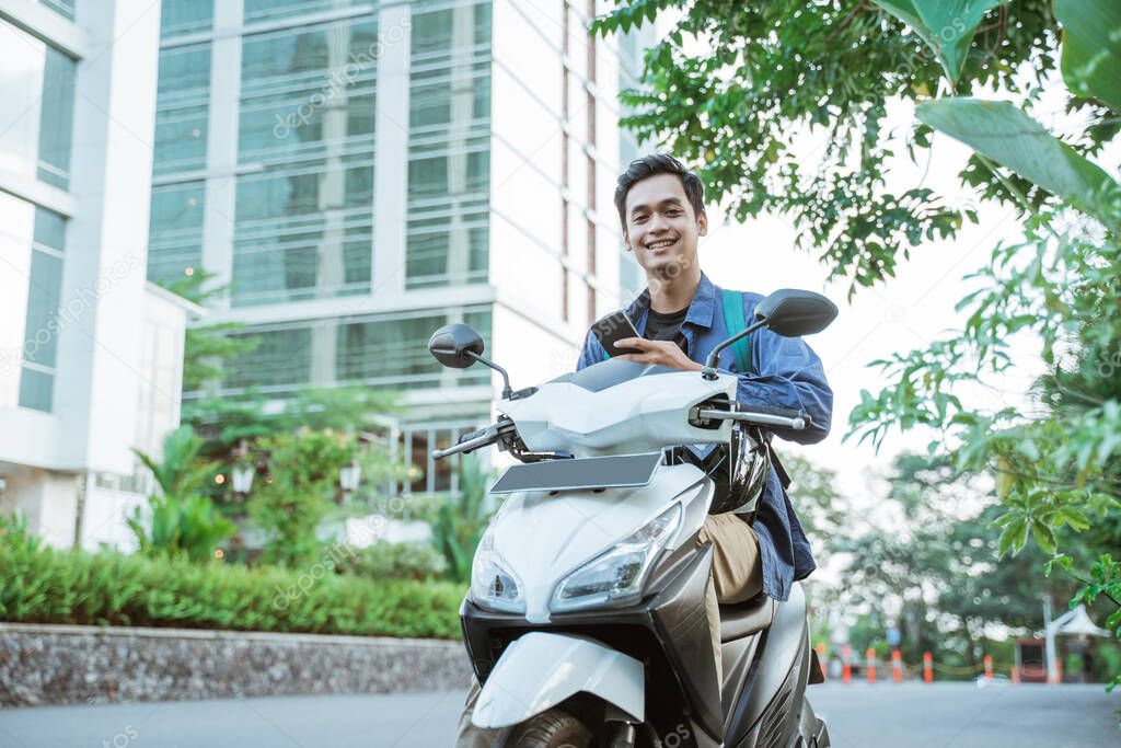 Smiling young man using a cellphone when riding a motorcycle