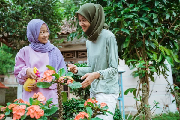 Ibu dan anak perempuan di kerudung mengobrol sambil menyemprotkan bunga tanaman — Stok Foto