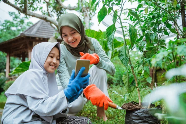 Anya és lánya mobiltelefont használ kertészkedés közben — Stock Fotó