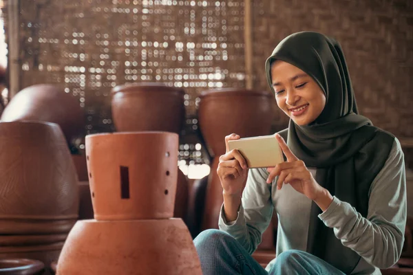 Dívka v hidžábu pomocí mobilního telefonu fotografovat hliněné produkty — Stock fotografie