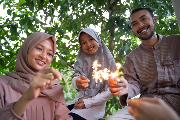 Sorrindo pai, mãe e filha acendendo fogos de artifício juntos — Fotografia de Stock