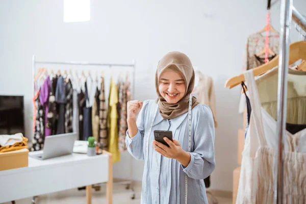 Збуджена азіатська мусульманка власник малого бізнесу дивиться на телефон — стокове фото