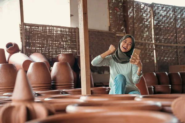 Překvapená muslimská dívka v hidžábu mezi keramikou při použití mobilního telefonu — Stock fotografie