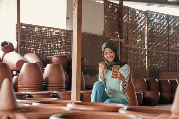 Šťastný muslim dívka v hidžábu mezi keramikou při použití mobilního telefonu — Stock fotografie