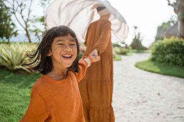 Müslüman anne ve kızı birlikte yürüyor ve el ele tutuşuyorlar.