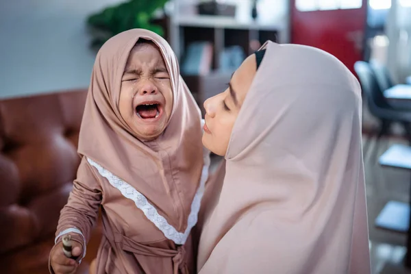 Мусульманская мать с шарфом хиджаба утешая свою плачущую маленькую девочку — стоковое фото