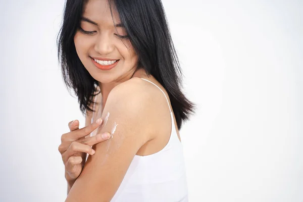 Ung kvinna applicerar grädde på armen. På en vit bakgrund. — Stockfoto