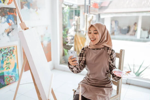 Moslim vrouwelijke kunstenaar op zoek naar inspiratie uit haar mobiele telefoon — Stockfoto