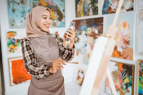 Artista femenina musulmana en busca de inspiración de su teléfono móvil —  Fotos de Stock