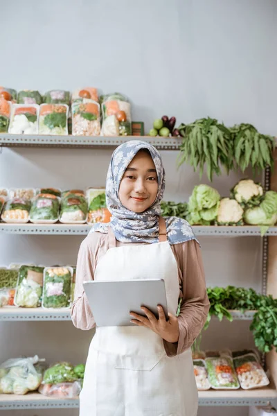 Chica en pañuelo para la cabeza la venta de verduras sonriendo con una almohadilla — Foto de Stock