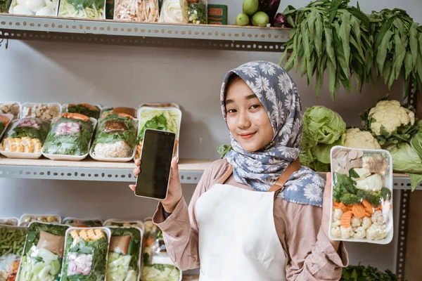 Mujer en hiyab vendiendo verduras mostrando verduras y pantalla móvil — Foto de Stock