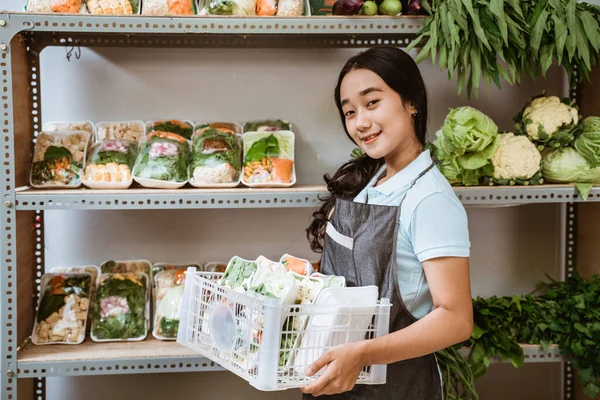 Glimlachende jonge vrouw met een schort vol groenten. — Stockfoto