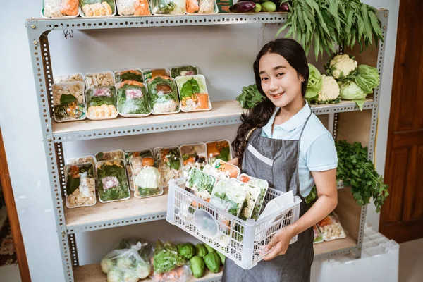 Glimlachende aziatische vrouw dragen schort dragen mand van verse groenten — Stockfoto