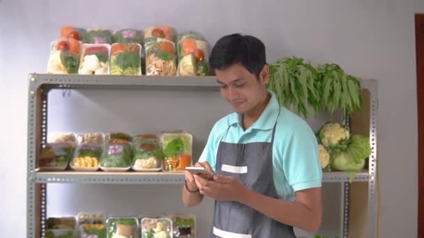 Asiatico maschio greengrocer mostrando verdure e mostrando uno schermo del telefono — Video Stock