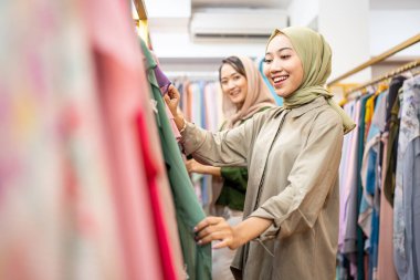 Müslüman kadın arkadaşıyla moda mağazasından yeni elbiseler alıyor.