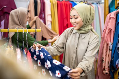 Müslüman kadın arkadaşıyla moda mağazasından yeni elbiseler alıyor.