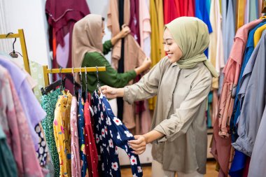 Müslüman kadın arkadaşıyla moda mağazasından yeni elbiseler alıyor.