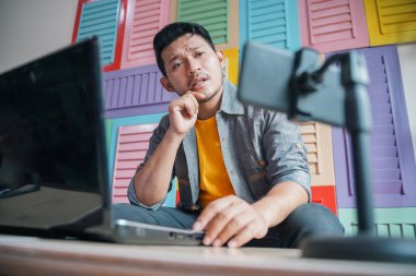 Adam dizüstü bilgisayarını kullanırken cep telefonuyla video çekiyor.