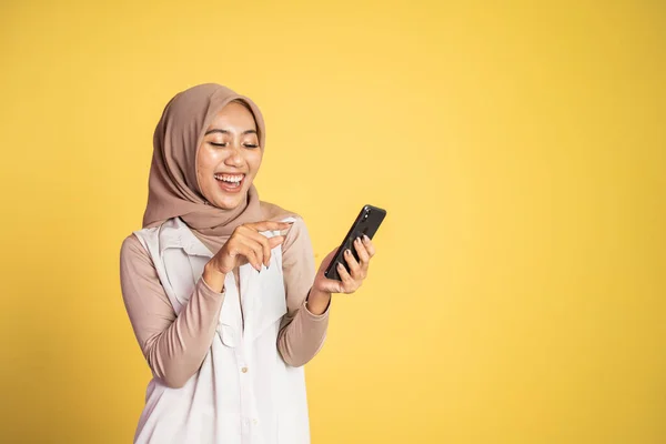 Мусульманская женщина смеется над своим смартфоном изолированным на желтый — стоковое фото