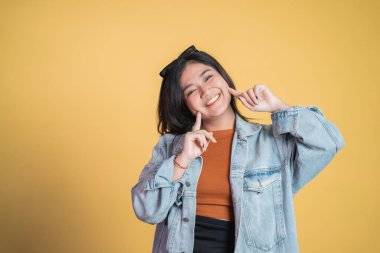 Yanağını gösteren iki parmağıyla gülümseyen tatlı bir genç kadın.