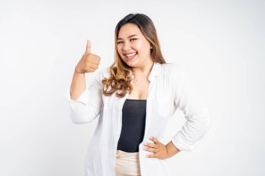 Gülümseyen genç bir kadın, soyutlanmış arka planda başparmağıyla duruyor.