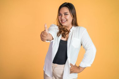 Gülümseyen genç bir kadın, soyutlanmış arka planda başparmağıyla duruyor.