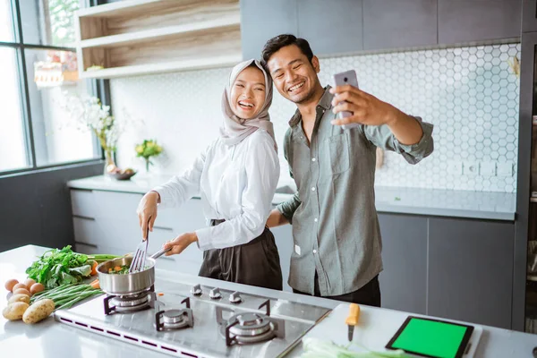 Мусульманська пара готує свою їжу на кухні і приймає селфі — стокове фото