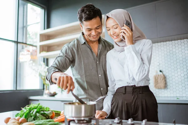 Мусульманська пара готує свою їжу на кухні, а дружина телефонує — стокове фото