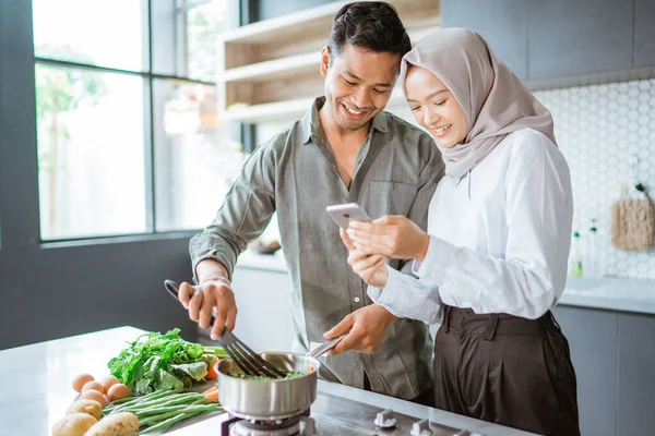 Casal muçulmano cozinhar juntos na cozinha, enquanto olha para o vídeo — Fotografia de Stock