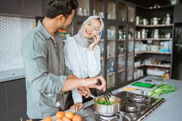 Casal muçulmano cozinhar sua comida na cozinha, enquanto a esposa tomar um telefonema — Fotografia de Stock